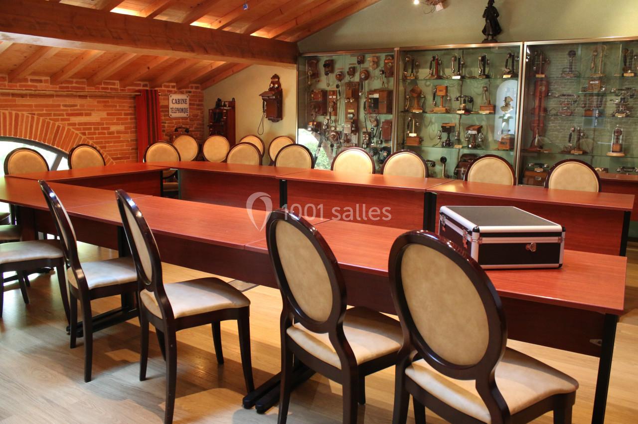 Salle de réunion avec des tables en bois disposées en U, des chaises rembourrées et une vitrine remplie de trophées.