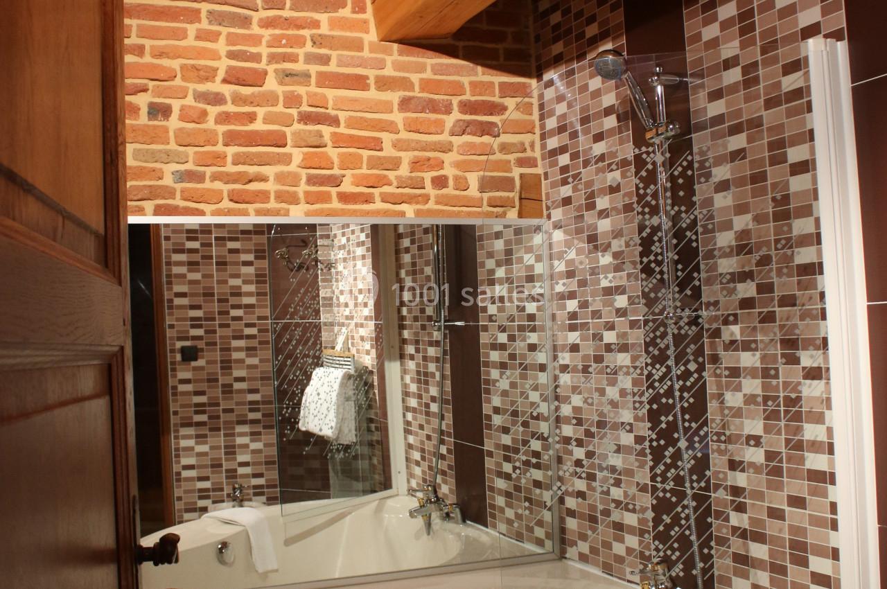 Salle de bain avec baignoire d'angle, mur en briques et carrelage mosaïque, sous un plafond en bois.