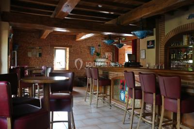 Table de billard en bois avec tapis vert dans une pièce au style rustique, avec poutres apparentes et murs en briques.