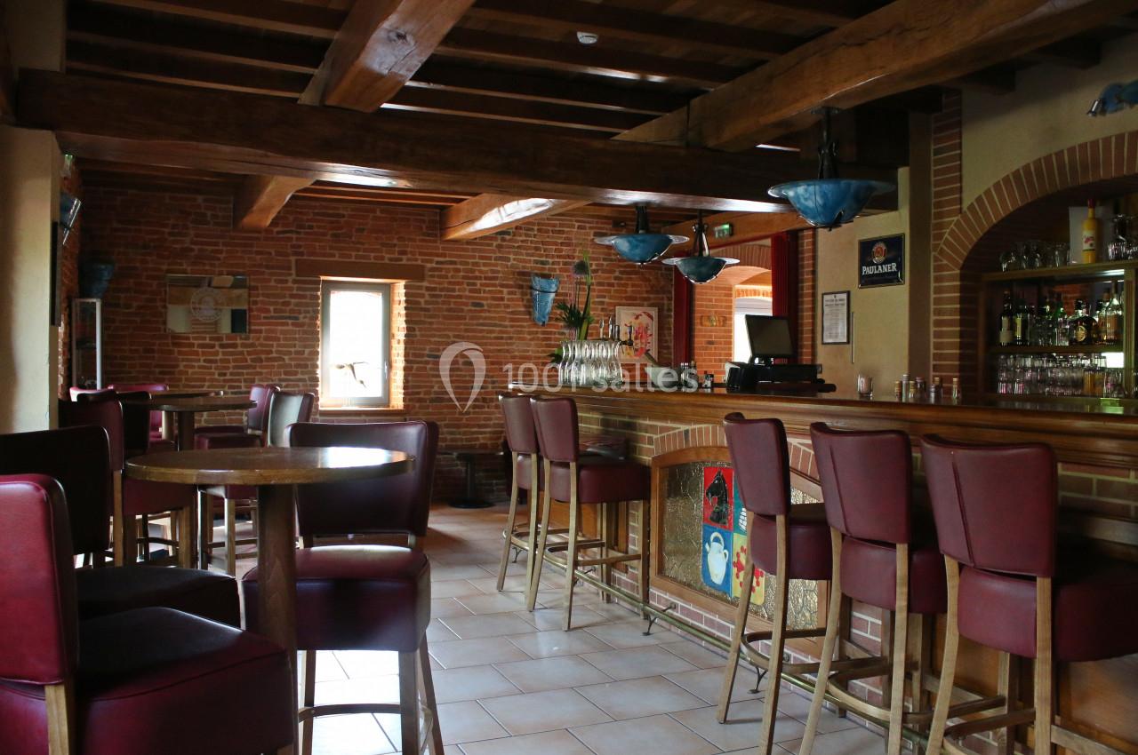 Intérieur d'un bar avec comptoir en bois, tabourets rouges, murs en briques et éclairage suspendu.