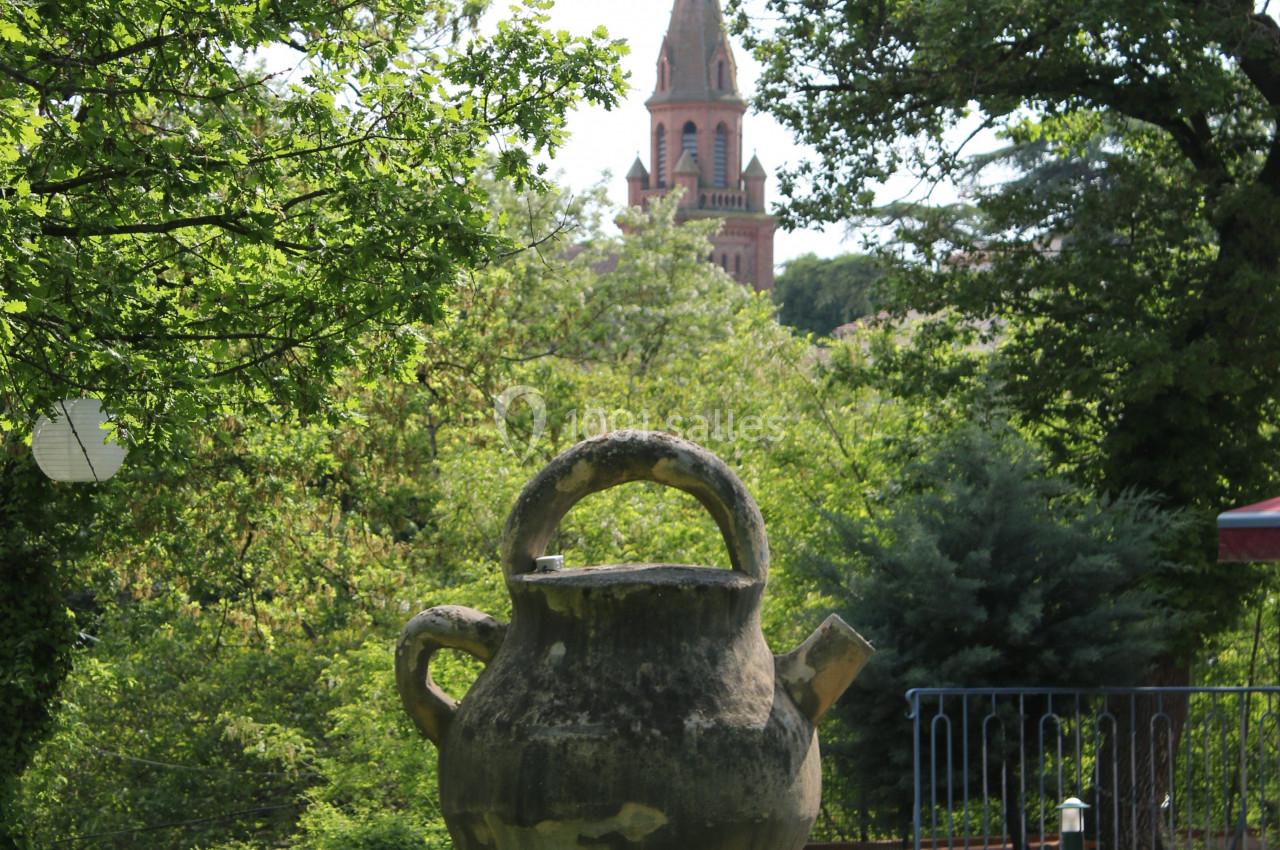 Grande jarre en pierre dans un parc verdoyant, avec une église en arrière-plan sous un ciel clair.