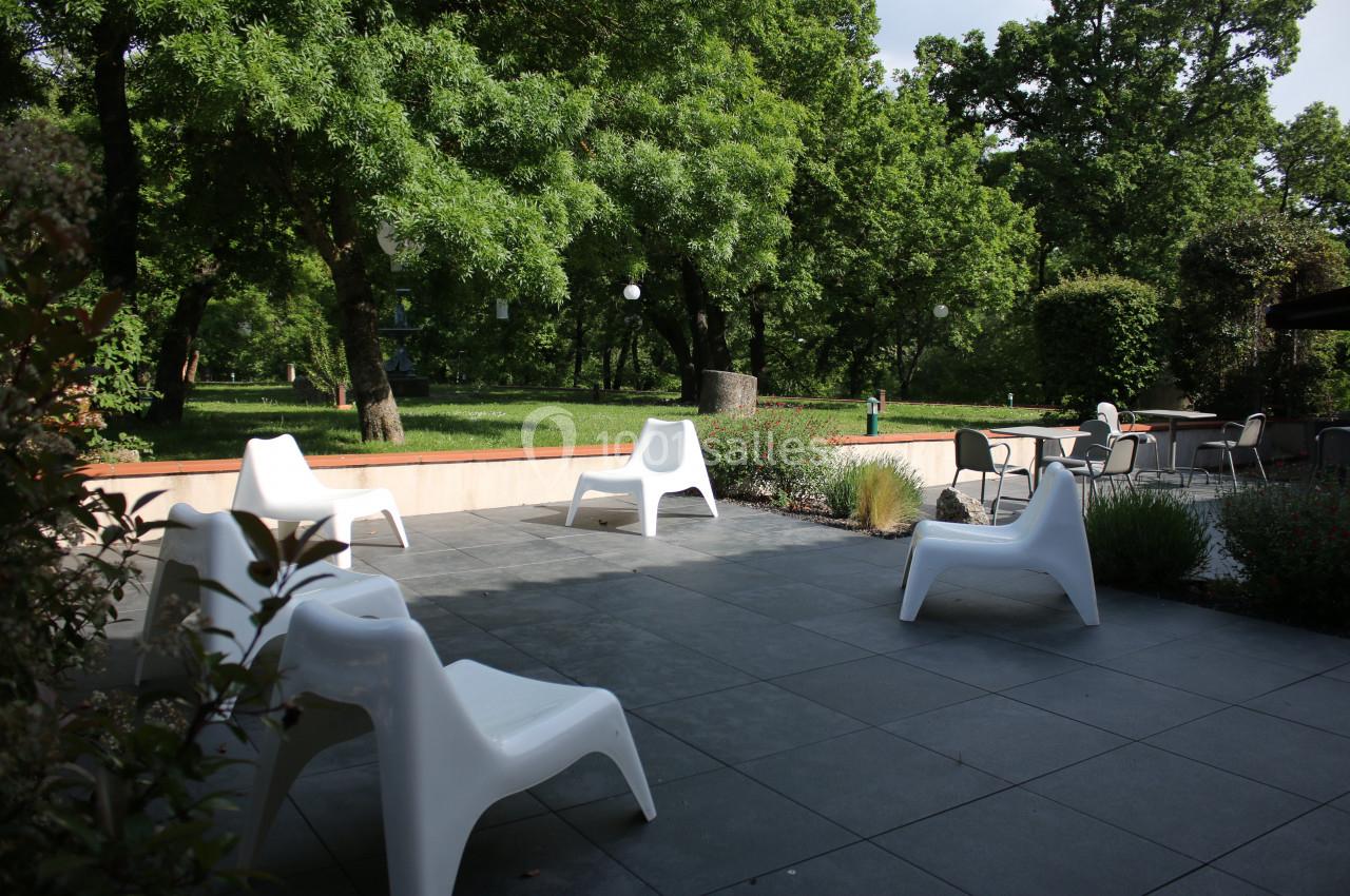Terrasse avec chaises blanches modernes, entourée de verdure et d'arbres, sous une lumière naturelle.