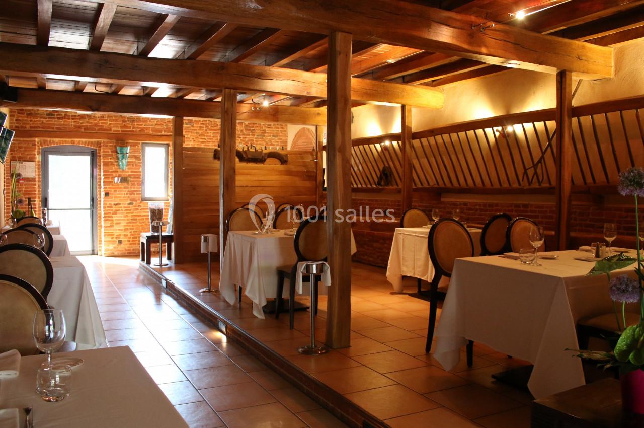 Salle de restaurant chaleureuse avec tables dressées, chaises en bois et murs en briques apparentes.
