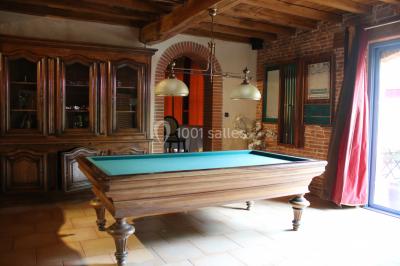 Table de billard en bois avec tapis vert dans une pièce au style rustique, avec poutres apparentes et murs en briques.