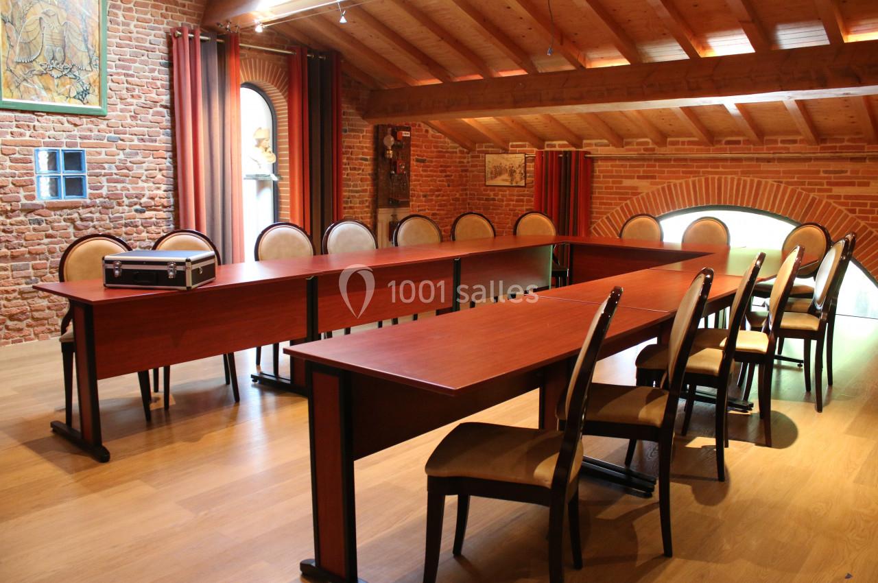 Salle de réunion avec tables en bois disposées en U, chaises rembourrées et murs en briques apparentes.