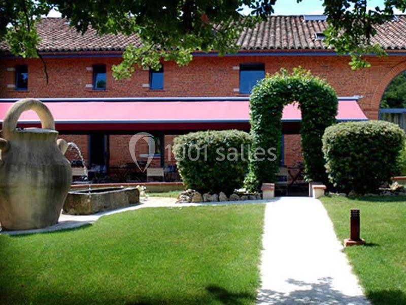 Façade en briques rouges d'une maison avec jardin, allée centrale, arbustes taillés et grande jarre décorative.