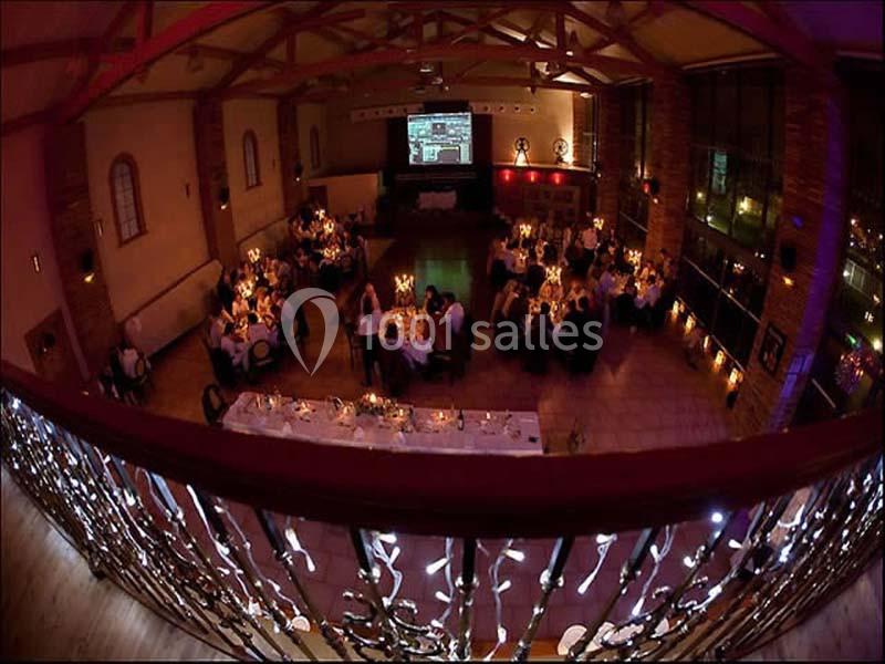 Salle de réception décorée avec des tables éclairées par des bougies, vue depuis une mezzanine ornée de motifs métalliques.