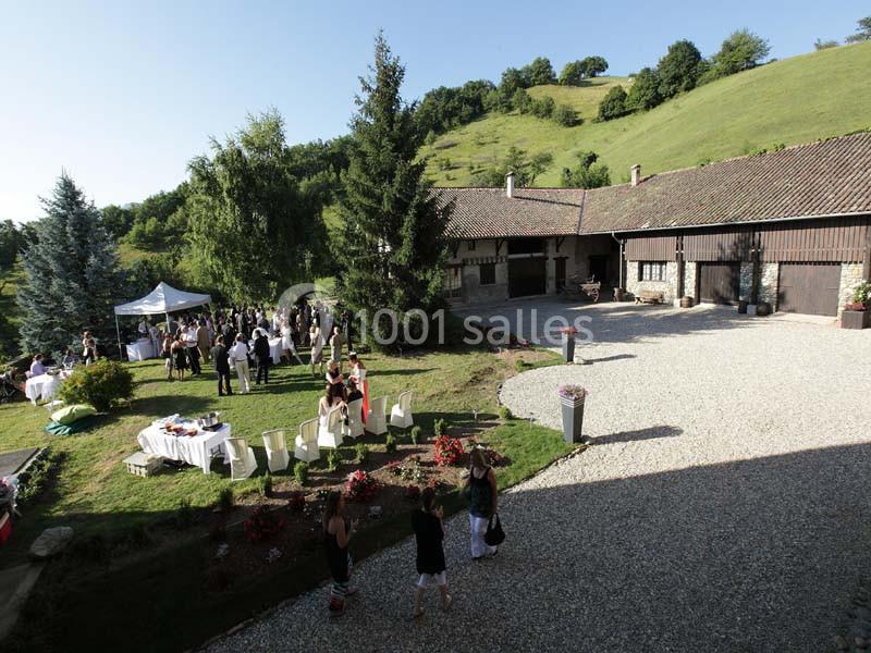 Vue d'une cour de ferme avec des invités réunis pour un événement en extérieur, entourée de verdure et de collines.