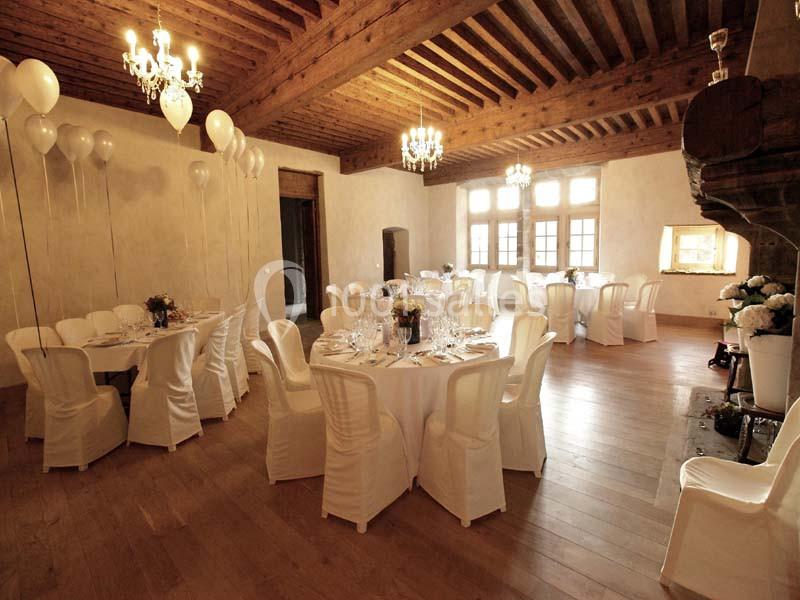 Salle de réception lumineuse avec tables rondes dressées, chaises blanches et décorations de ballons blancs.