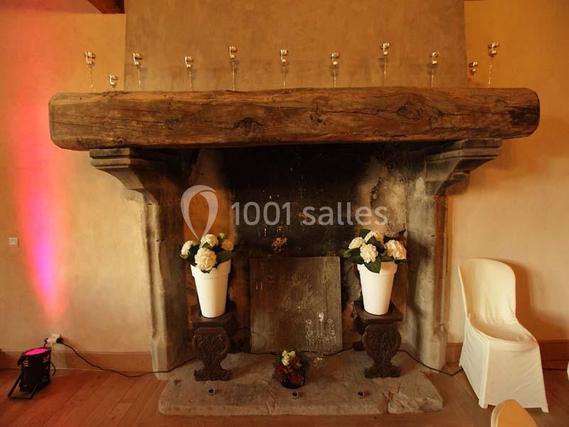 Cheminée ancienne en pierre avec poutre en bois, décorée de vases blancs contenant des fleurs et des bougies alignées.