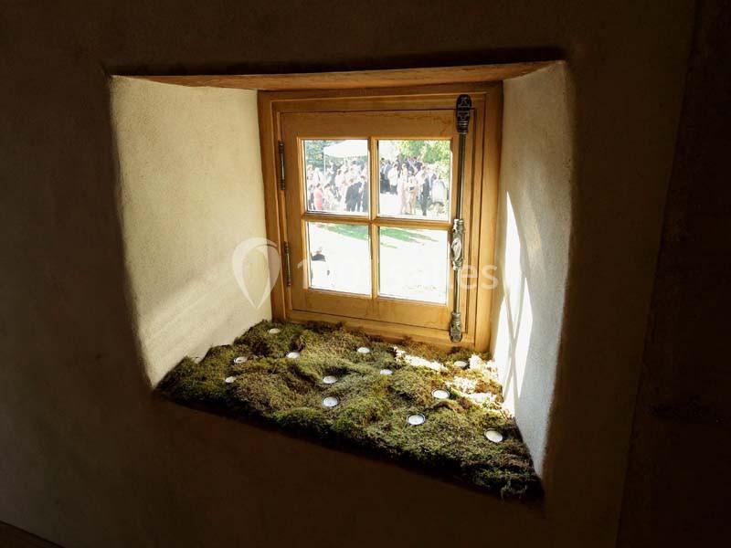 Fenêtre en bois éclairée par la lumière naturelle, avec un rebord recouvert de mousse et de petites bougies.