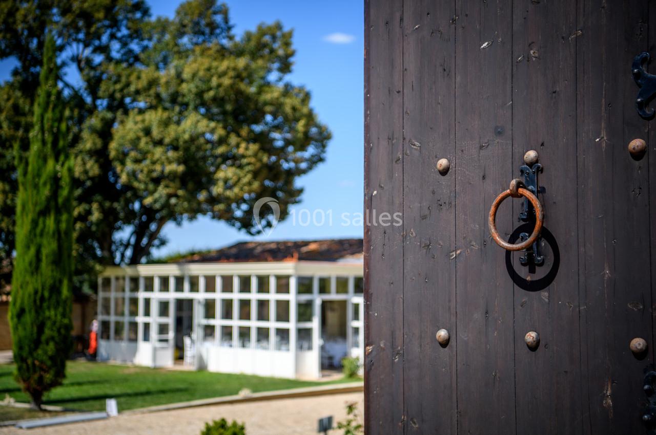 Porte en bois sombre avec anneau en métal au premier plan, jardin et bâtiment vitré en arrière-plan.