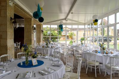 Une mariée en robe blanche marche sur une terrasse en bois, un enfant ajuste son voile sous un ciel dégagé.