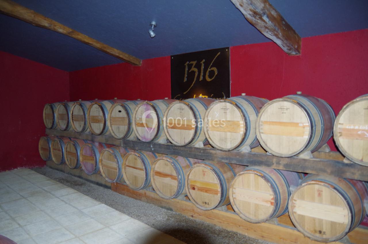 Rangées de tonneaux en bois alignés dans une cave à vin aux murs rouges et plafond sombre.