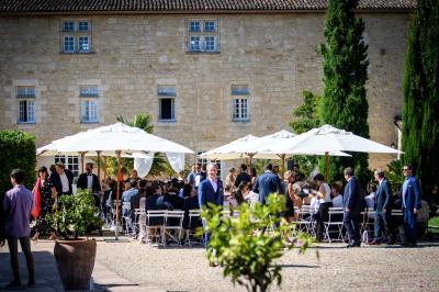 Une mariée en robe blanche marche sur une terrasse en bois, un enfant ajuste son voile sous un ciel dégagé.