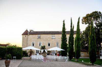 Une mariée en robe blanche marche sur une terrasse en bois, un enfant ajuste son voile sous un ciel dégagé.