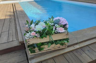 Une mariée en robe blanche marche sur une terrasse en bois, un enfant ajuste son voile sous un ciel dégagé.