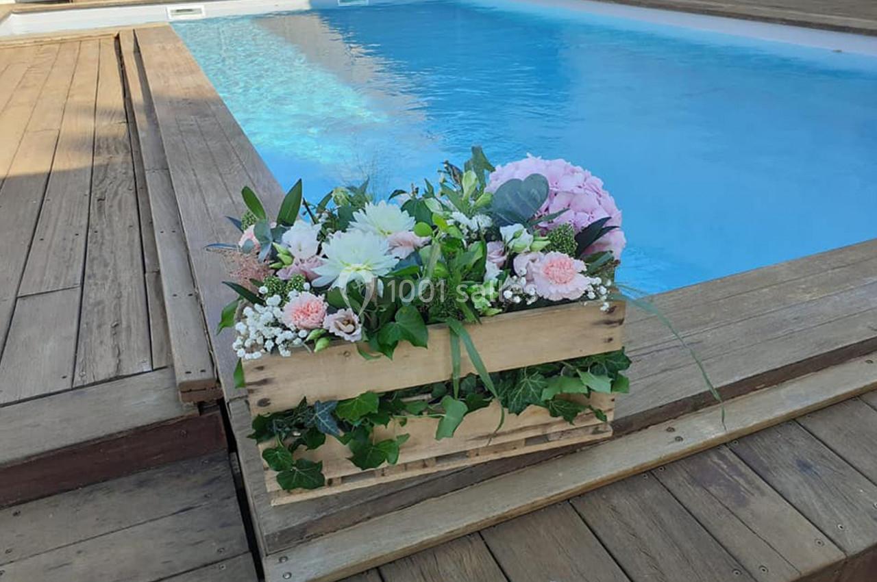 Arrangement floral dans une caisse en bois posé sur une terrasse en bois près d'une piscine.