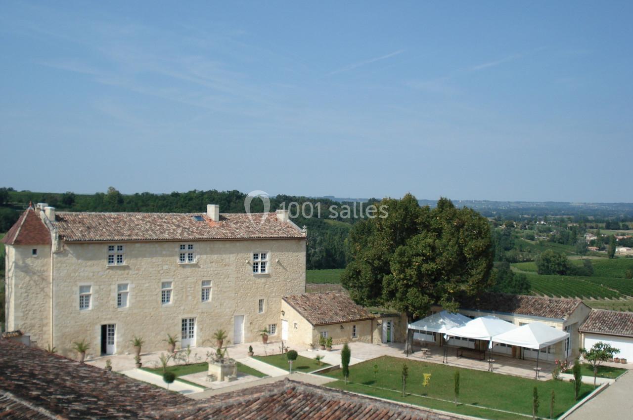 Vue d'un bâtiment en pierre entouré de jardins, avec des collines verdoyantes à l'arrière-plan.