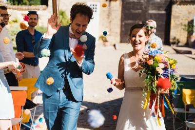 Une mariée en robe blanche marche sur une terrasse en bois, un enfant ajuste son voile sous un ciel dégagé.