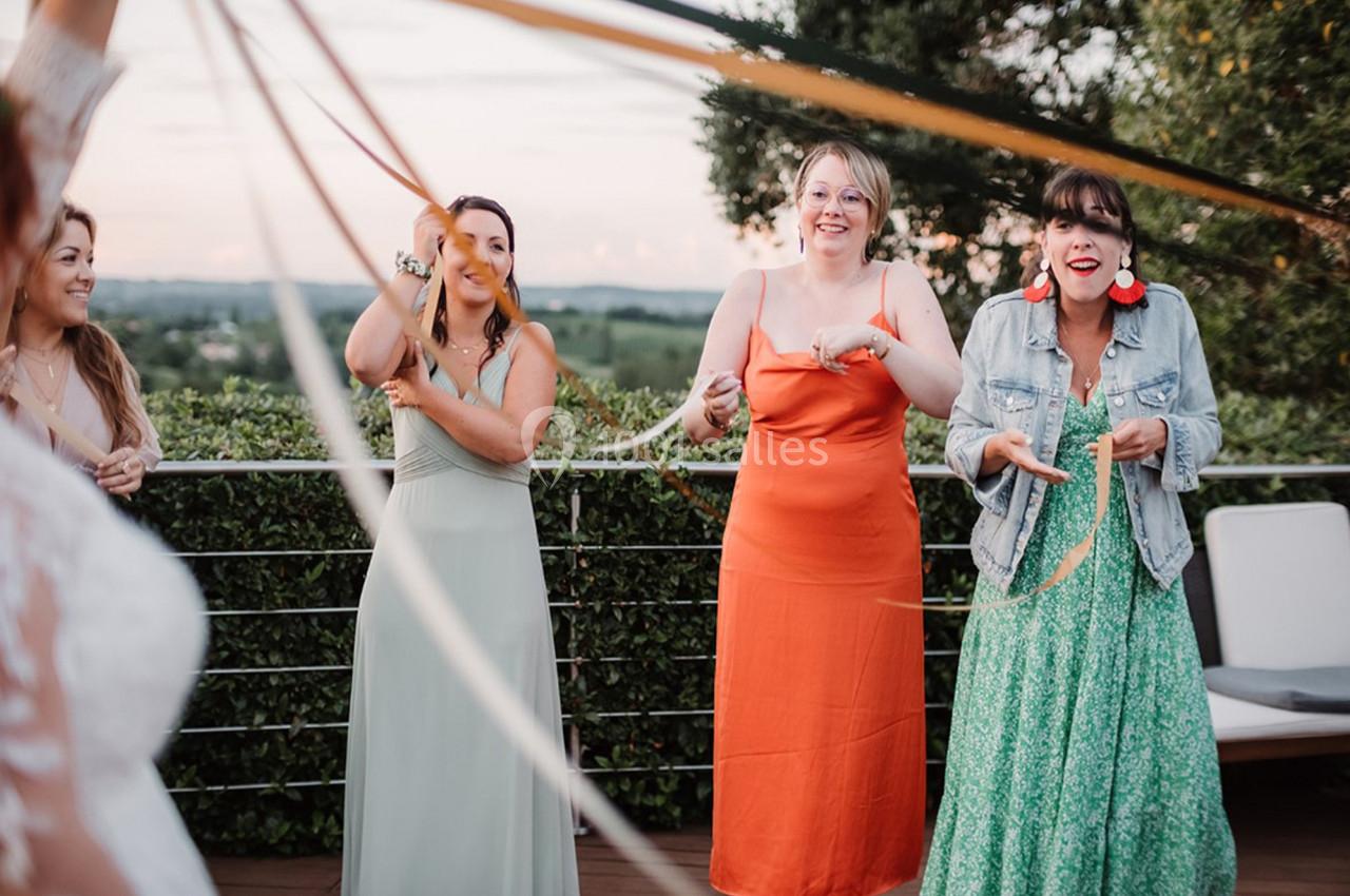 Des femmes souriantes participent à une activité festive en extérieur, tenant des rubans colorés tendus.