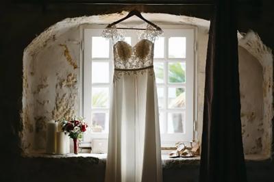 Une mariée en robe blanche marche sur une terrasse en bois, un enfant ajuste son voile sous un ciel dégagé.