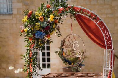 Une mariée en robe blanche marche sur une terrasse en bois, un enfant ajuste son voile sous un ciel dégagé.