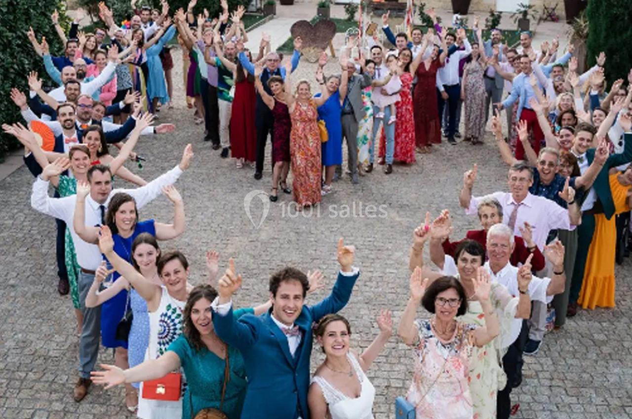 Un grand groupe de personnes souriantes, habillées élégamment, posant en extérieur avec les bras levés.