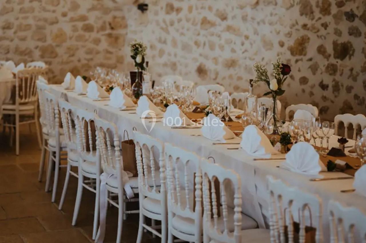 Grande table de banquet décorée avec nappes blanches, serviettes pliées et vaisselle, dans une salle en pierre.