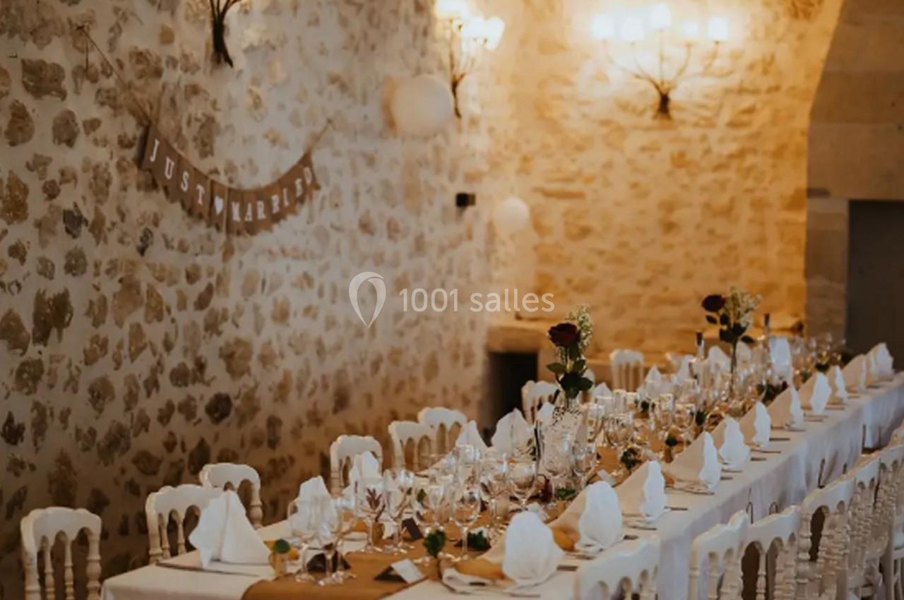 Table décorée pour un mariage dans une salle en pierre, avec nappes blanches, vaisselle élégante et fleurs.