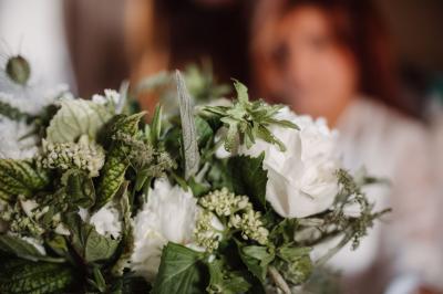 Une mariée en robe blanche marche sur une terrasse en bois, un enfant ajuste son voile sous un ciel dégagé.