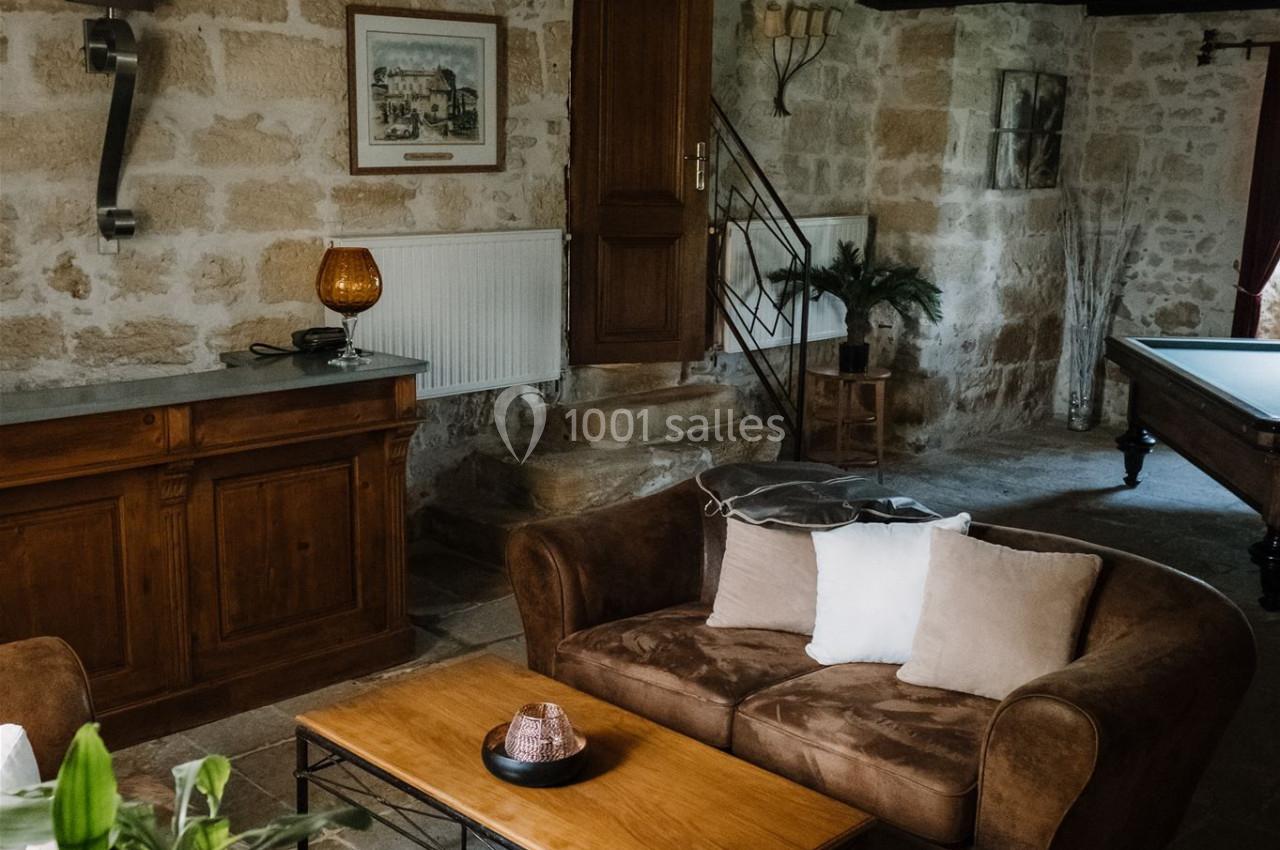 Salon rustique avec murs en pierre, poutres apparentes, canapé en velours brun, table basse en bois et décoration…