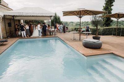 Une mariée en robe blanche marche sur une terrasse en bois, un enfant ajuste son voile sous un ciel dégagé.