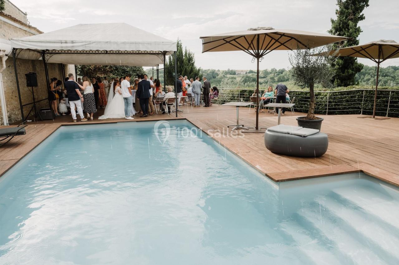 Groupe de personnes rassemblées près d'une piscine et sous une tente, dans un cadre extérieur avec vue sur la campagne.