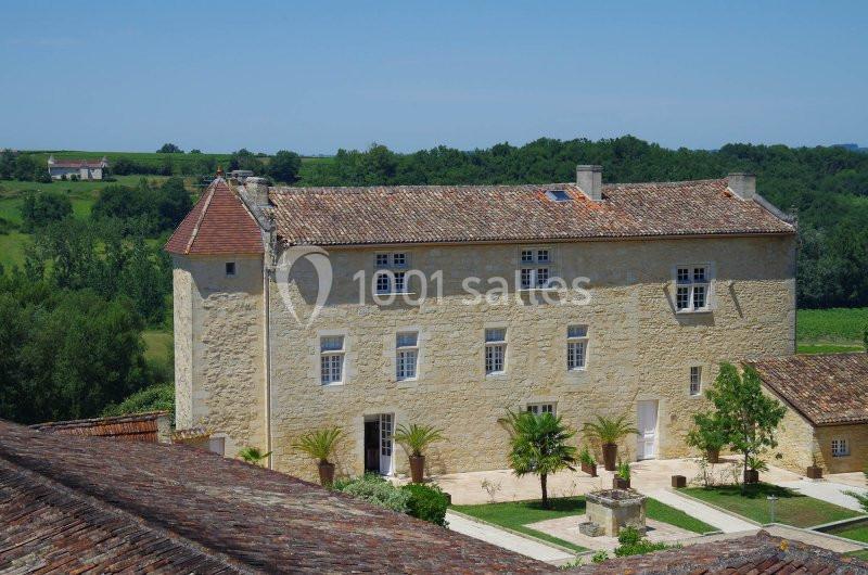 Vue d'un bâtiment en pierre de style traditionnel entouré de verdure, avec une cour et des palmiers au premier plan.
