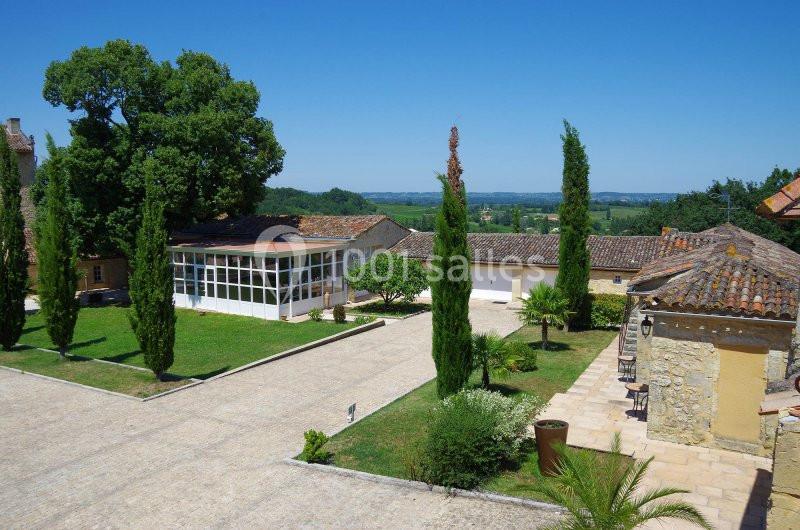 Cour pavée avec arbres et bâtiments en pierre, entourée de verdure et offrant une vue sur la campagne.