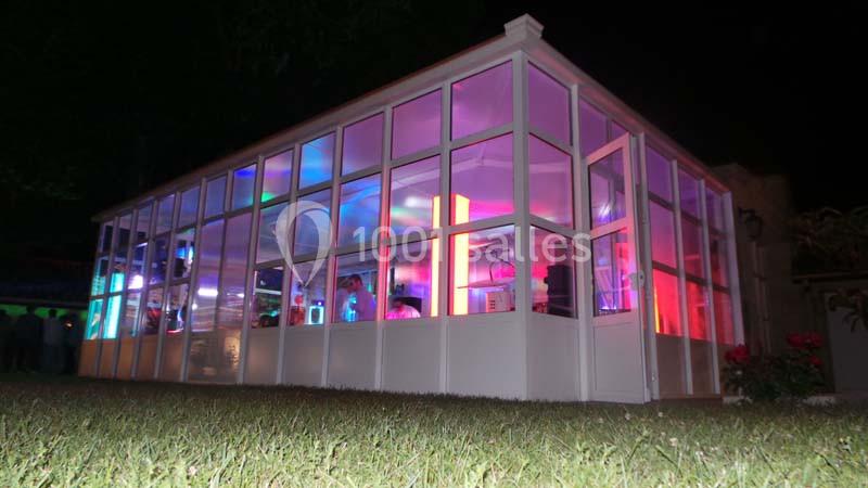 Verrière illuminée de nuit avec des lumières colorées visibles à l'intérieur, entourée de pelouse.