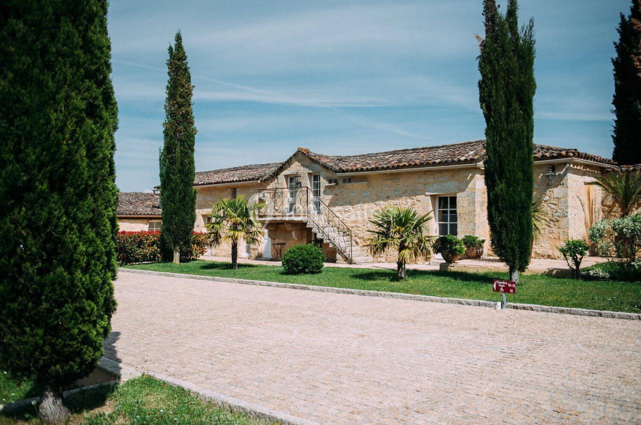Bâtisse en pierre avec escalier extérieur, entourée de cyprès et de végétation, sous un ciel bleu clair.