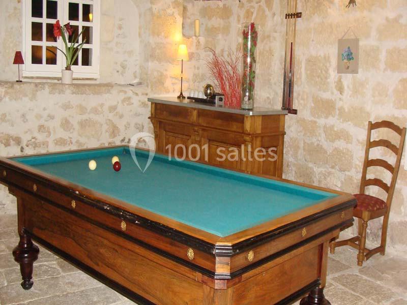 Table de billard en bois dans une pièce en pierre avec une fenêtre, une commode et des décorations murales.
