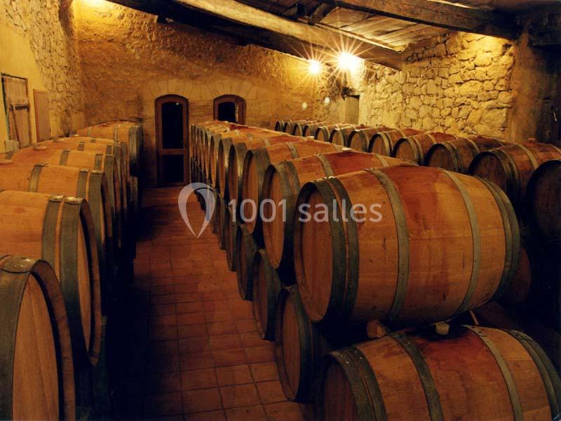 Rangées de fûts en bois alignés dans une cave en pierre éclairée par des lumières chaudes.