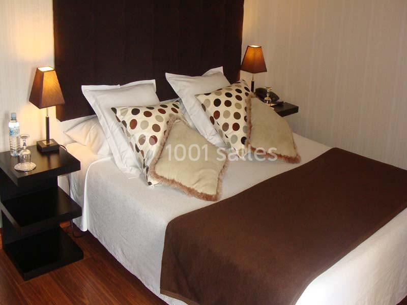 Lit double avec coussins décoratifs à motifs, couverture marron, lampes de chevet et tables noires dans une chambre.