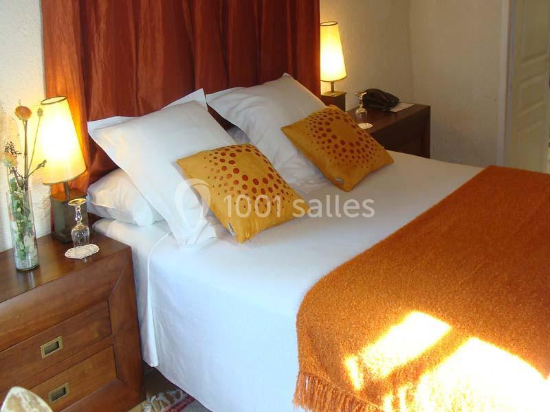 Lit double avec draps blancs, coussins décoratifs jaunes, plaid orange, lampes de chevet allumées et mobilier en bois.