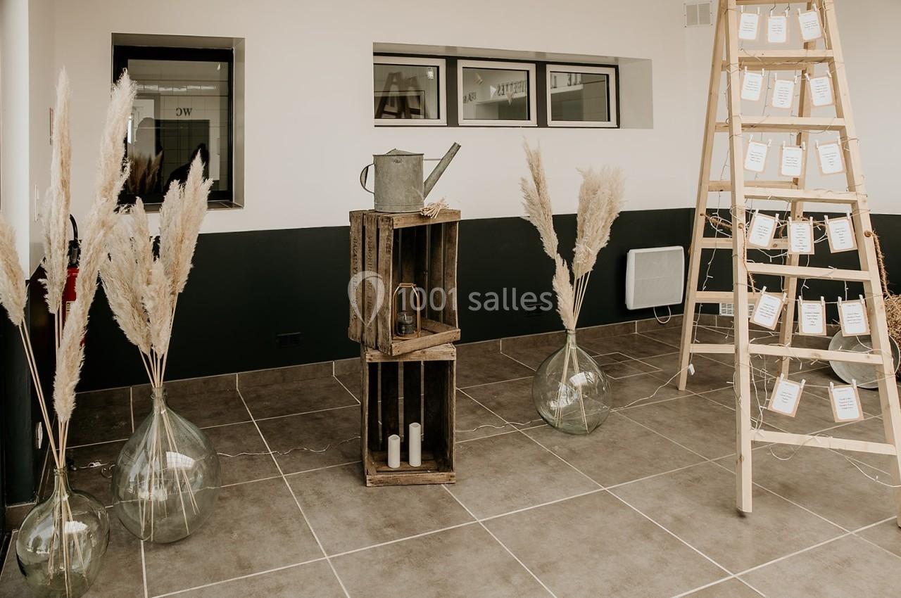 Décoration intérieure avec échelle en bois portant des cartes, vases de pampas et caisses en bois sur un sol carrelé.