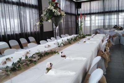 Salle de réception décorée avec des tables dressées, nappes blanches, chemins de table en jute et chaises noires.
