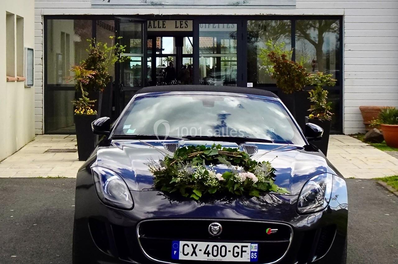 Voiture noire décorée de fleurs devant une salle de réception avec enseigne ’Salle des Guifettes’.