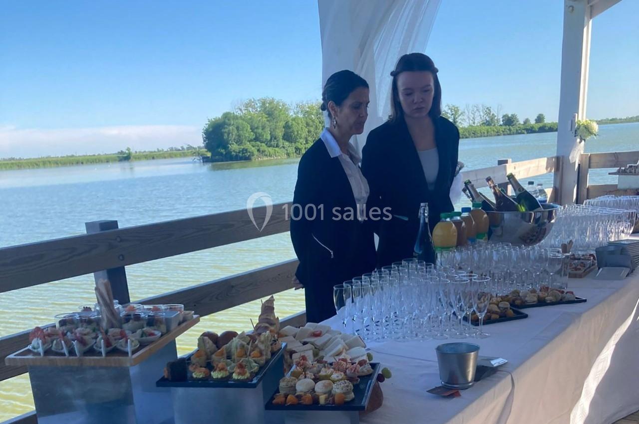 Deux personnes devant une table dressée avec des amuse-bouches, des boissons et des verres, près d'un plan d'eau.