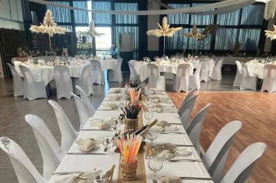 Salle de réception décorée avec des tables dressées, nappes blanches, chemins de table en jute et chaises noires.