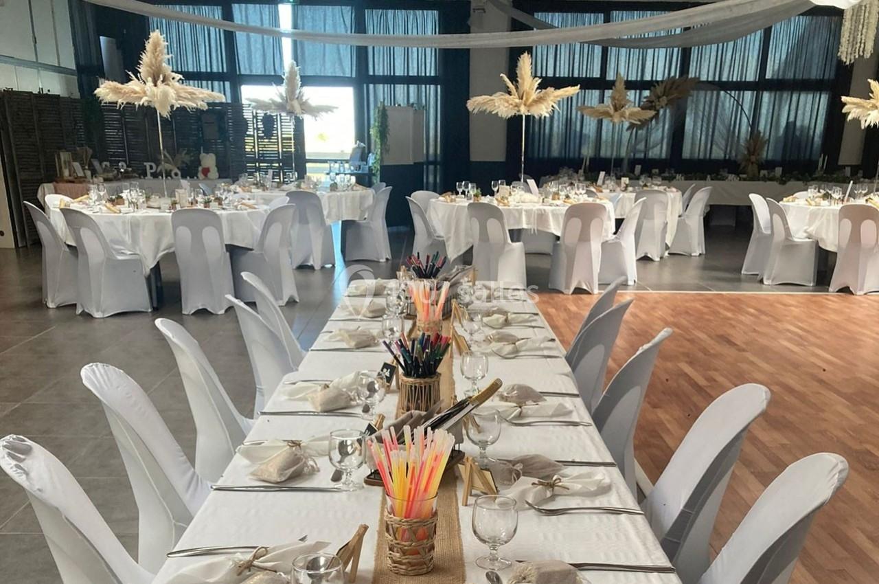 Salle de réception décorée avec des tables dressées, nappes blanches, chaises houssées et ornements en pampas.
