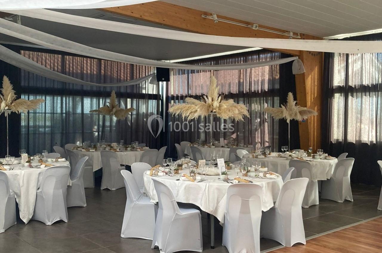 Salle de réception décorée avec des tables rondes, nappes blanches, chaises houssées et centres de table en pampas.