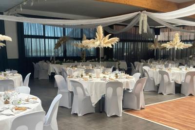 Salle de réception décorée avec des tables dressées, nappes blanches, chemins de table en jute et chaises noires.